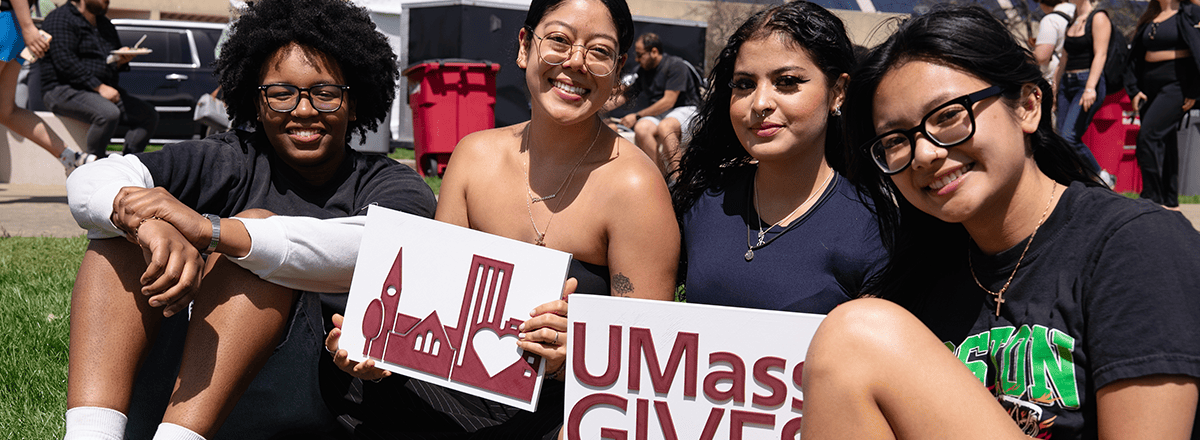 Students sitting on grass holding UMassGives signage