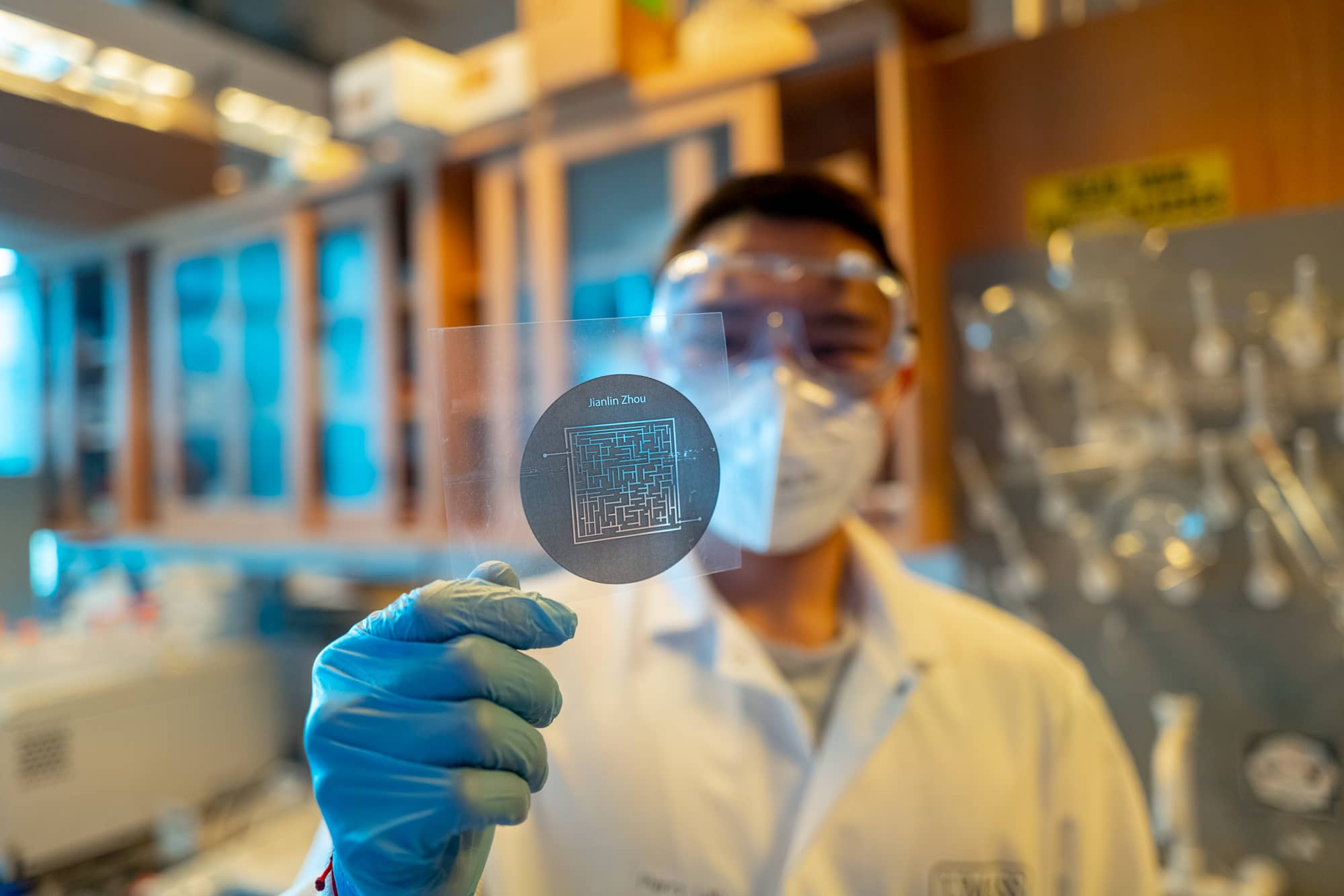 Student wearing mask holding up graphic in lab