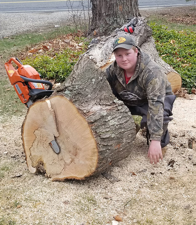 Ty Moughan faces camera posing next to large log with chainsaw.